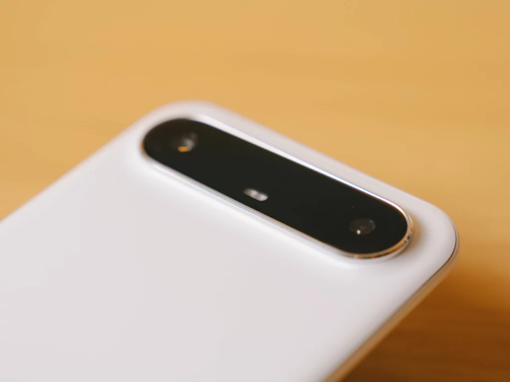 Close-up of the distinctive, elongated camera module on the white back of the TECNO SPARK Slim against a wooden and yellow background.