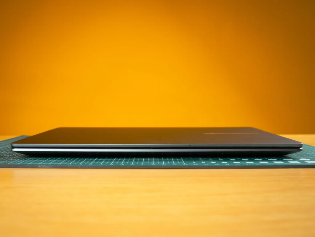 A side-profile close-up of the closed, thin ASUS ExpertBook laptop, resting on a green cutting mat. The laptop is closed and its slim profile is visible.