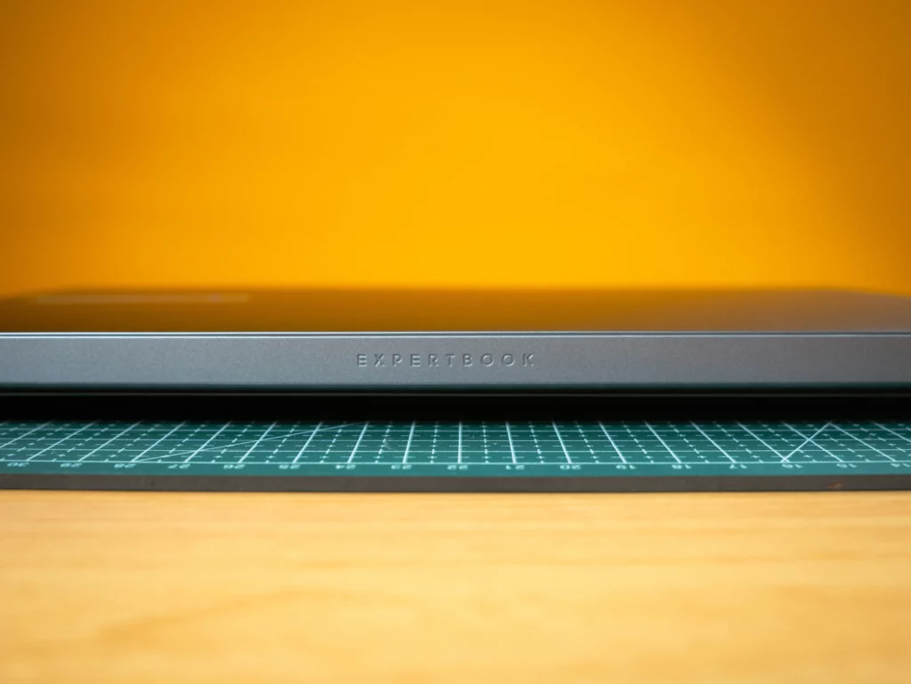 An extreme close-up of the front lip of the closed ASUS ExpertBook, with the word "EXPERTBOOK" subtly debossed or printed in the center. The laptop is resting on a green cutting mat.