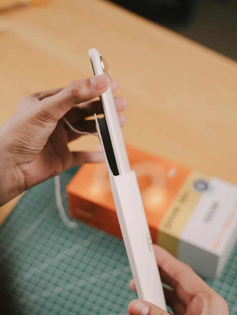 Hands sliding the white TECNO SPARK Slim smartphone out of its protective paper sleeve within the box.