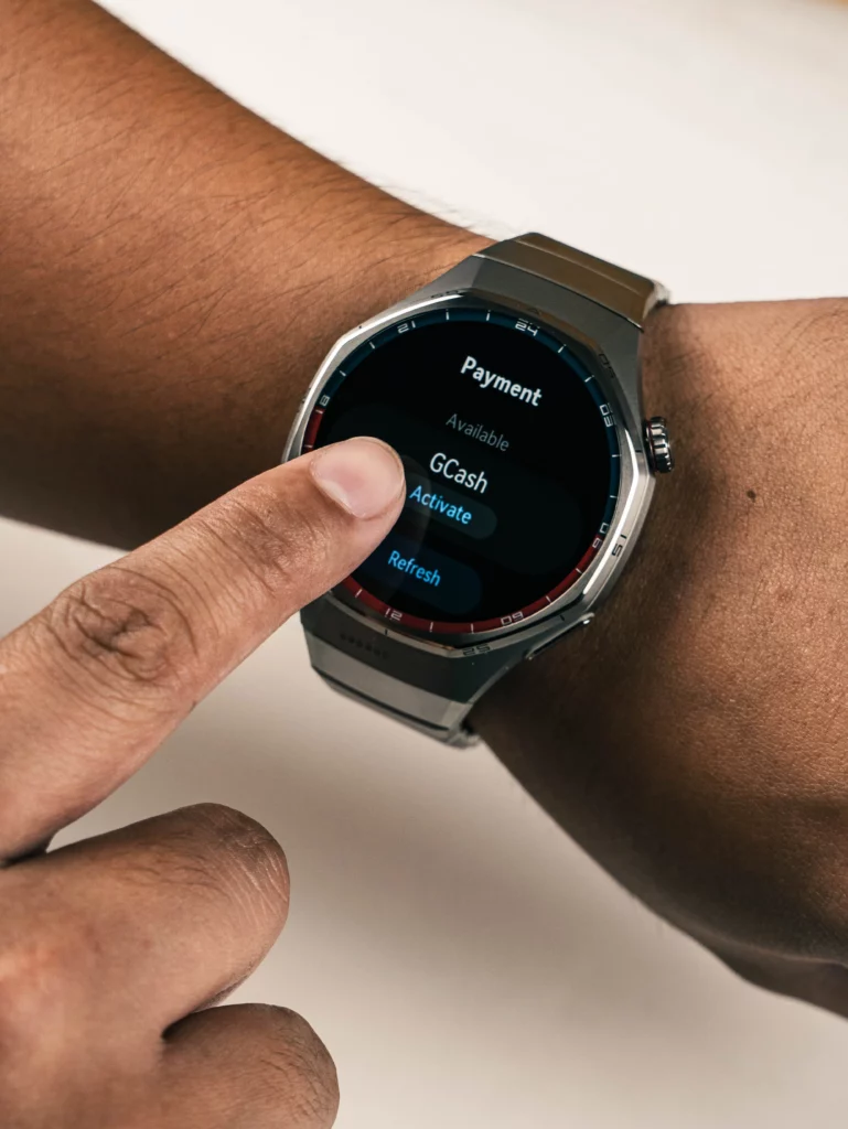 Close-up of a person's finger tapping the screen of the Huawei Watch GT 6 Pro. The watch is displaying a "Payment" menu with an "Available" option for GCash and an "Activate" button.