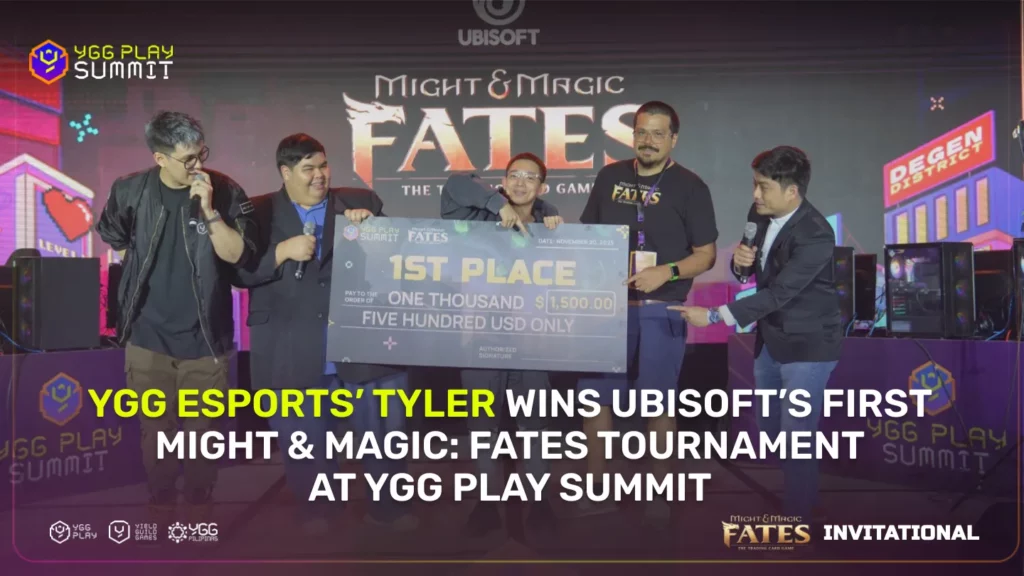 "Five people are standing on stage under the Ubisoft banner. YGG Esports player Tyler holds a large check for $1,500, celebrating his 1st place win in the Might & Magic: Fates tournament at the YGG Play Summit. 'DEGEN DISTRICT' is visible on the backdrop screen."