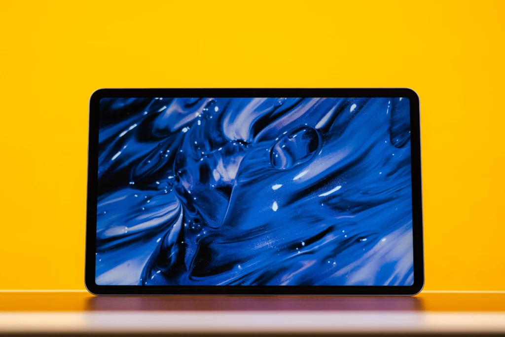 The front of the Infinix XPAD 20 Pro tablet displaying a bright, abstract blue and black liquid wallpaper, set against a bright yellow background.