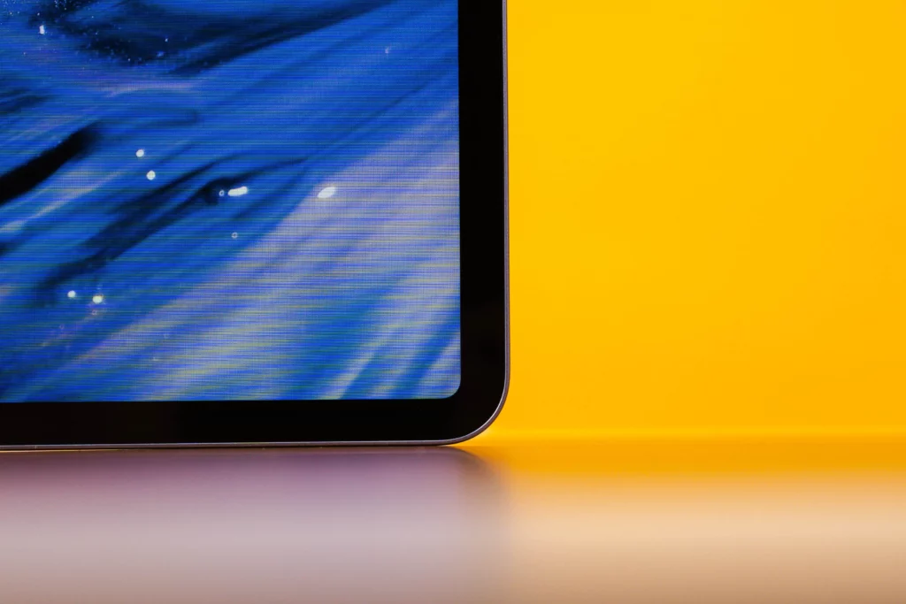 A close-up of the bottom right corner of the tablet's screen, showing a minimal bezel and the curved edge of the device, with a bright yellow background.