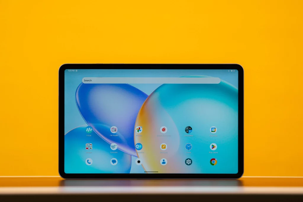 The Infinix XPAD 20 Pro tablet displaying its home screen with various app icons like FM Radio, Calculator, and Google, set against a bright yellow background.