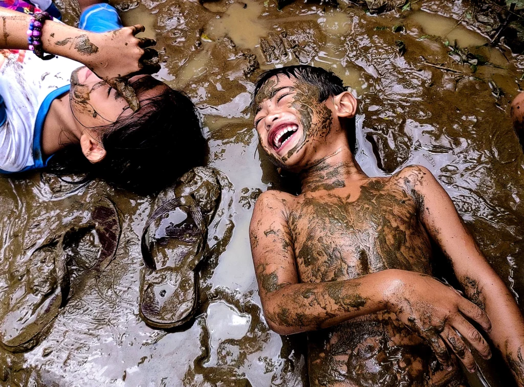 A close-up portrait of a young Filipino child smiling widely, their face covered in mud, embodying pure joy. (Photo by Mark Linel Padecio on HUAWEI nova 10)