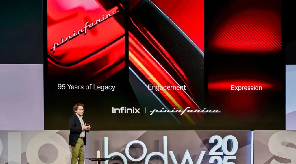 A wide photo taken at a conference showing a Pininfarina representative speaking on stage. The large screen behind him is split into three vertical sections detailing the new partnership: 1) "95 Years of Legacy" against a glossy red surface, 2) "Engagement" next to a textured red and yellow surface with carbon fiber accents, and 3) "Expression" next to a pattern of red carbon fiber. The co-branding logo "Infinix
