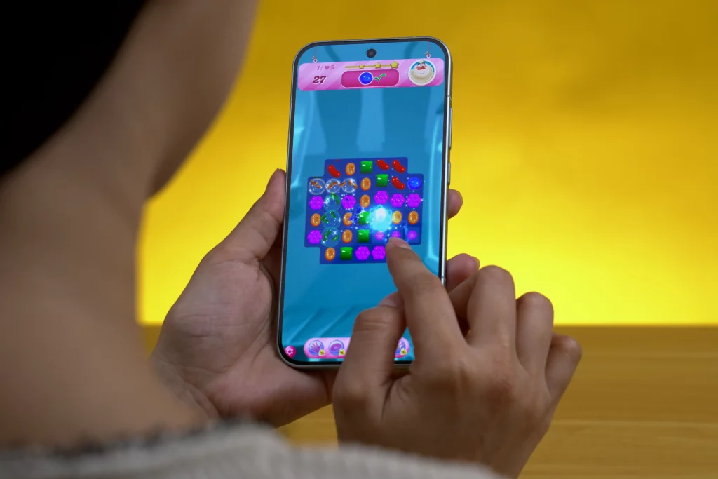 The POCO F8 Pro is held vertically by hands while a person plays the game Candy Crush Saga, touching the screen to match gems.