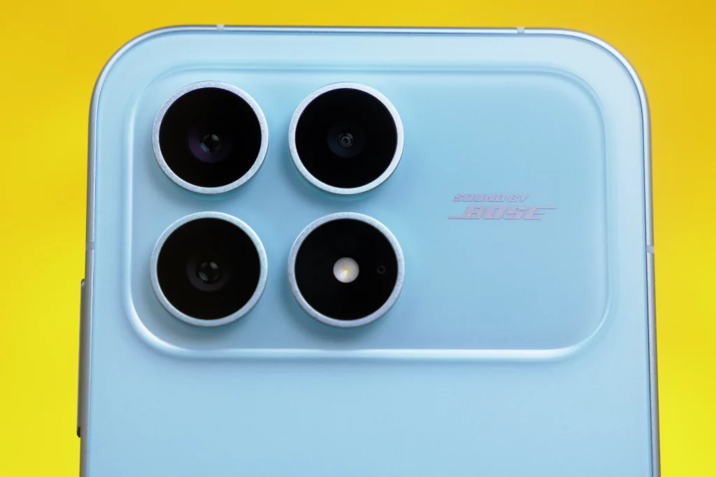 Close-up shot of the light blue, glossy back panel of the POCO F8 Pro smartphone, showing the four prominent circular camera lenses and the "SOUND BY BOSE" inscription etched into the glass.