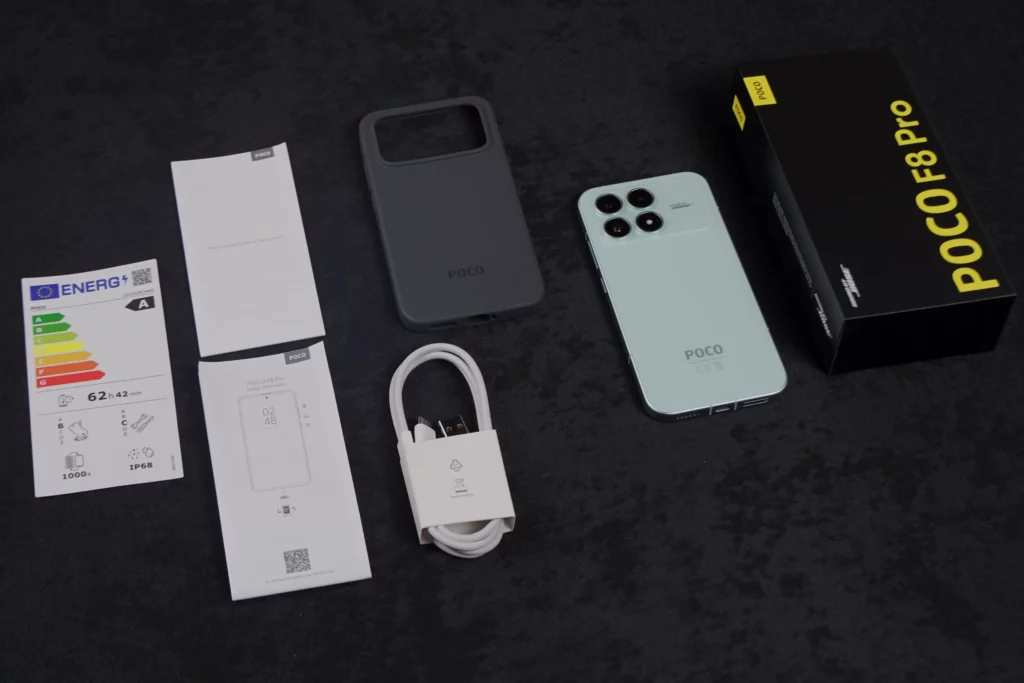 An overhead flat lay of the POCO F8 Pro unboxing contents: the light blue phone, black retail box, a dark gray protective case, a white USB cable, and several paper documents including a Quick Start Guide and an energy efficiency label.