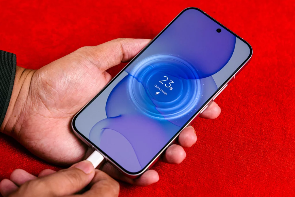 A close-up shot of a hand holding and plugging a charging cable into the bottom of the POCO F8 Ultra smartphone. The screen displays a purple quick charge animation with a "23%" battery level indicator. The phone is set against a red background.
