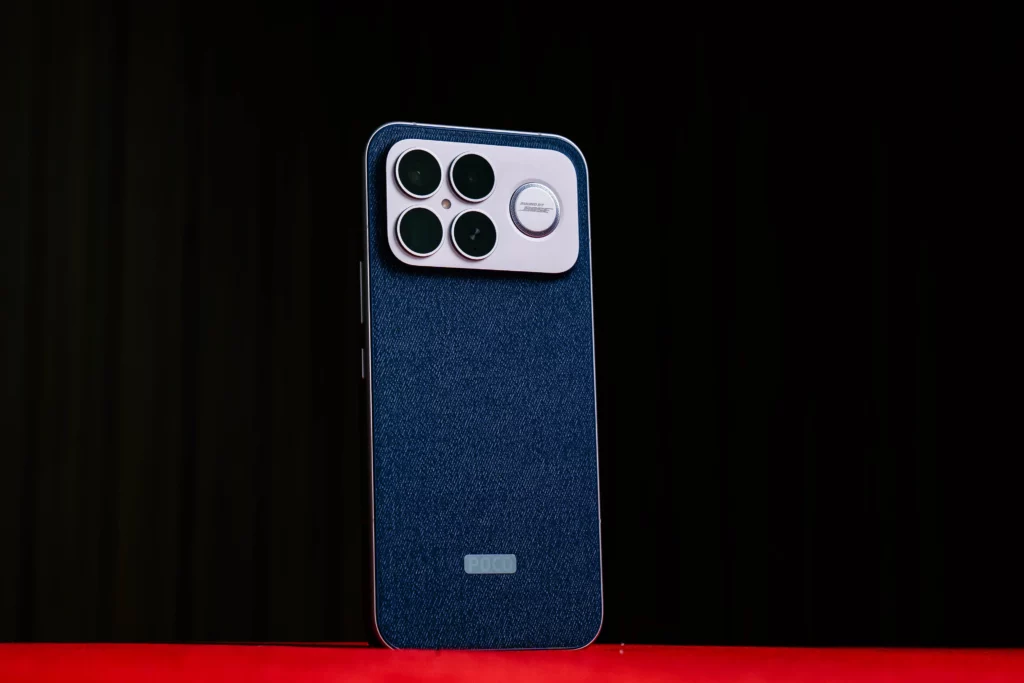 The back of the POCO F8 Ultra phone, with its distinctive blue textured finish and large, four-lens camera module, shown on a red surface with a dark background.