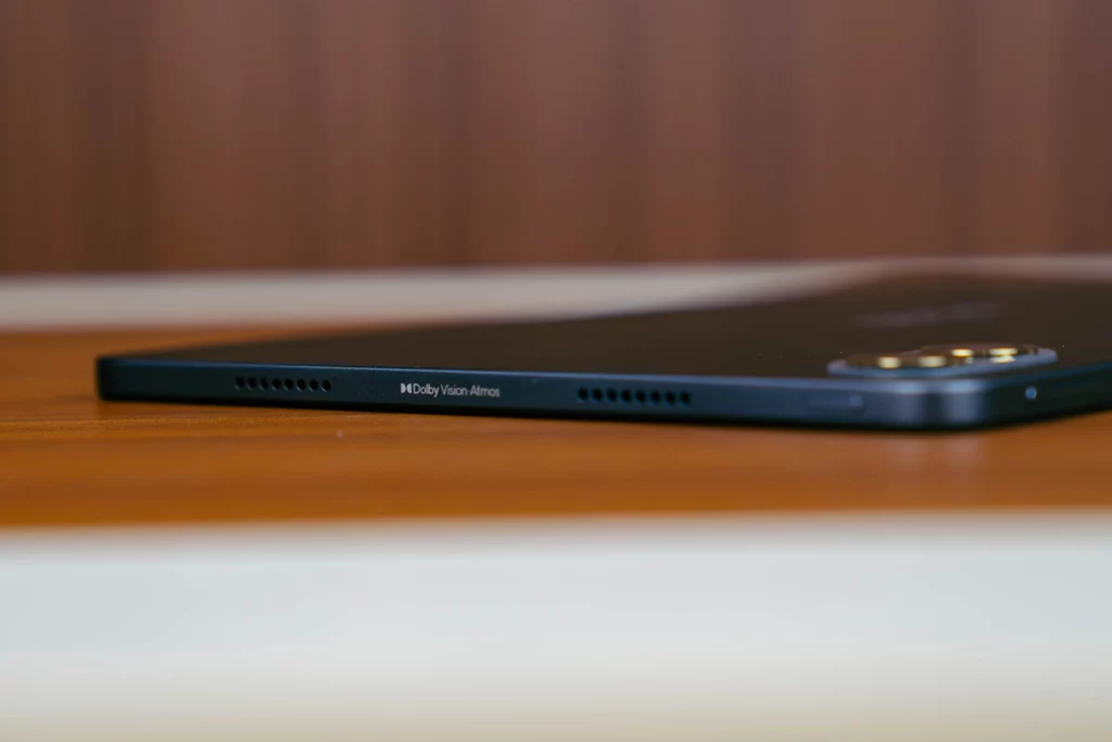 Close-up shot of the side edge of the POCO Pad M1 tablet, showing the speaker grille holes and the "Dolby Vision · Atmos" branding text, emphasizing its audio capabilities.