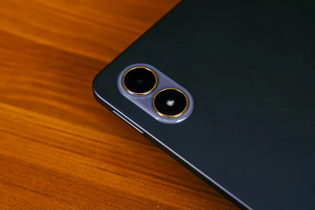 Close-up on the back of the dark gray POCO Pad M1 tablet, showing the distinctive pill-shaped rear camera module with two circular lenses highlighted by gold/yellow accents.