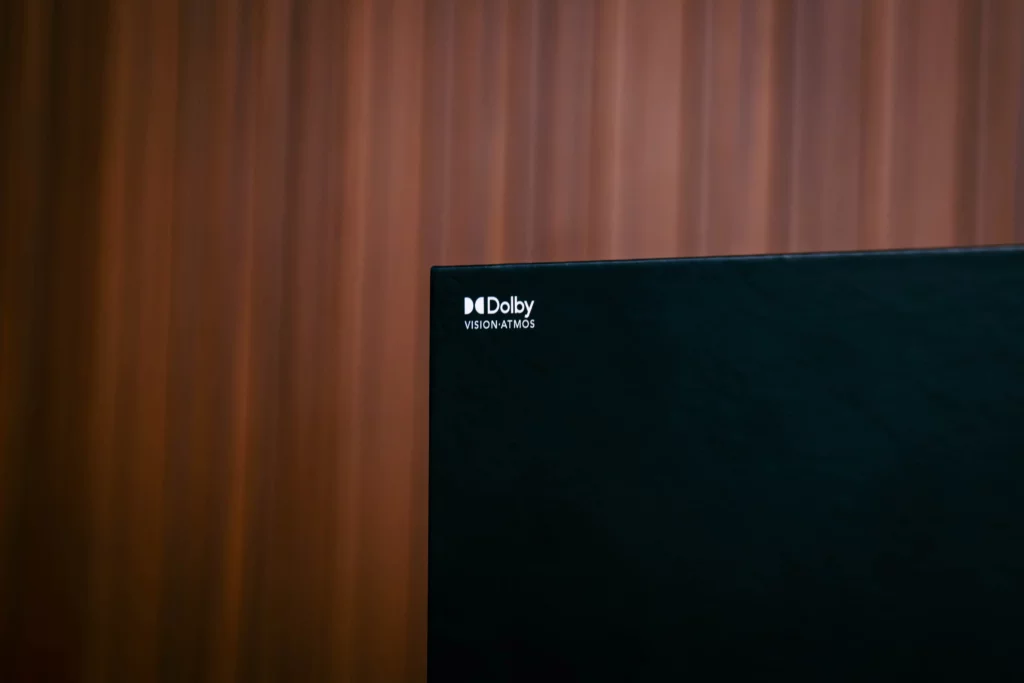 Close-up on the corner of the POCO Pad M1's black box, clearly showing the white "Dolby VISION · ATMOS" logo against a dark background with vertical wood grain paneling behind it.