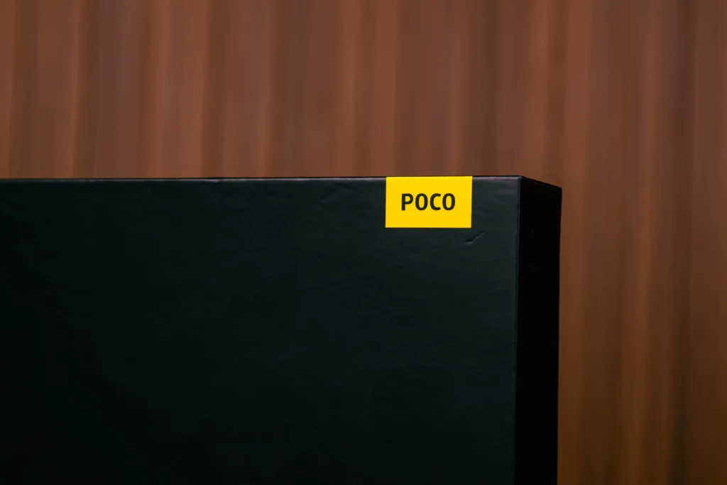 Close-up on the corner of the POCO Pad M1's black retail box, showing the small, yellow rectangular sticker with the word "POCO" printed on it.