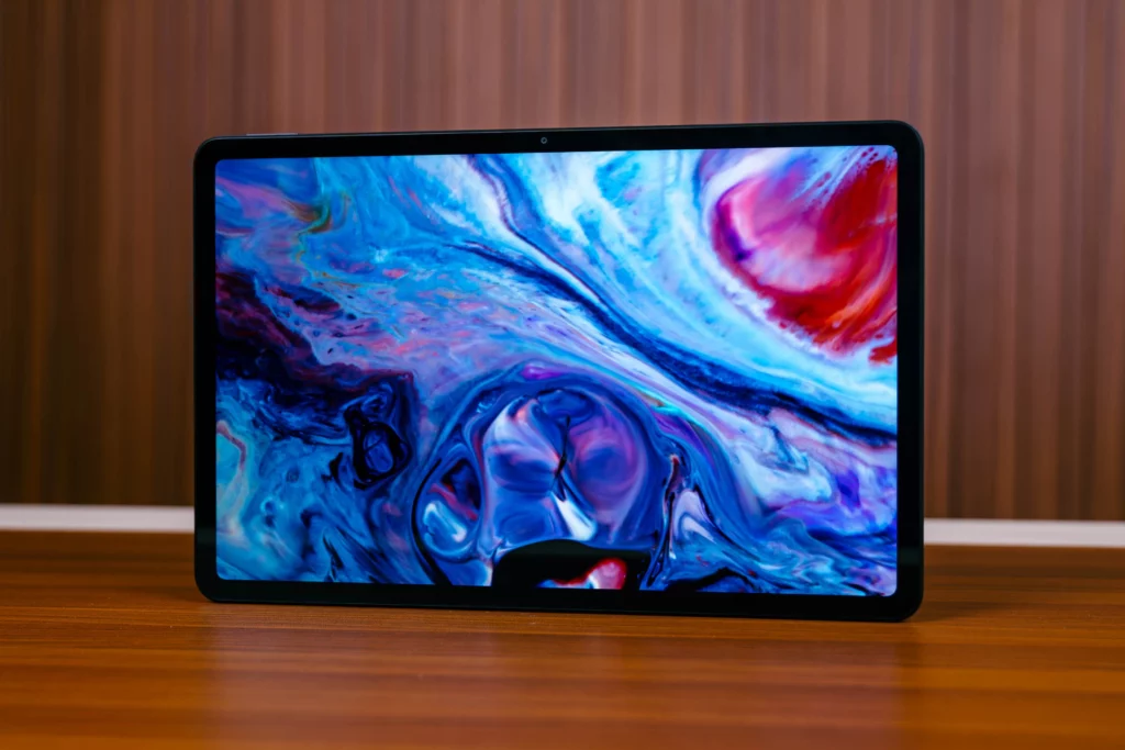 The POCO Pad M1 tablet standing on a wooden surface, displaying a vibrant, colorful, abstract liquid/marble-like pattern on its screen. The front-facing camera is visible above the screen.