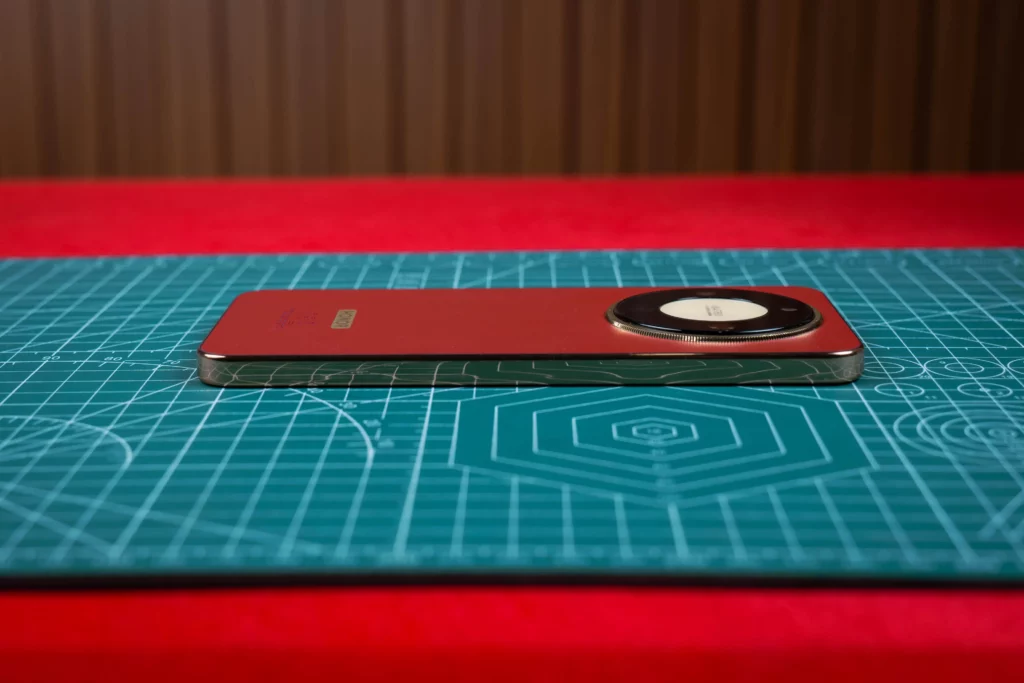 A side profile of the HONOR X9d 5G in Reddish Brown lying flat on a green cutting mat. The image highlights the phone's slim 7.76mm chassis and the prominent circular "Matrix" camera housing with a gold-textured rim.