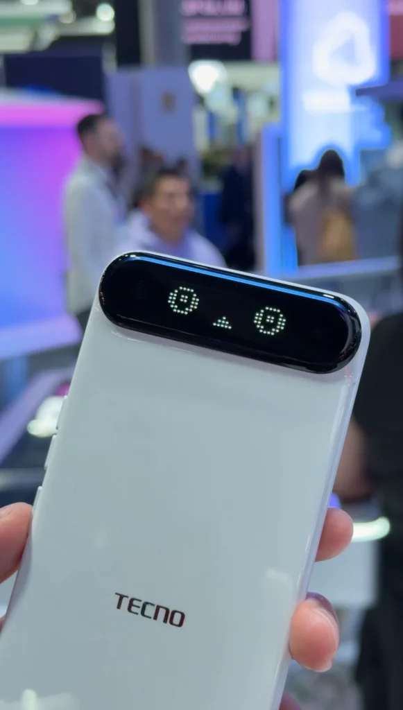 A tight close-up of the digital face on the back of the white Tecno phone. The LED "eyes" are animated with a pixelated, friendly expression.