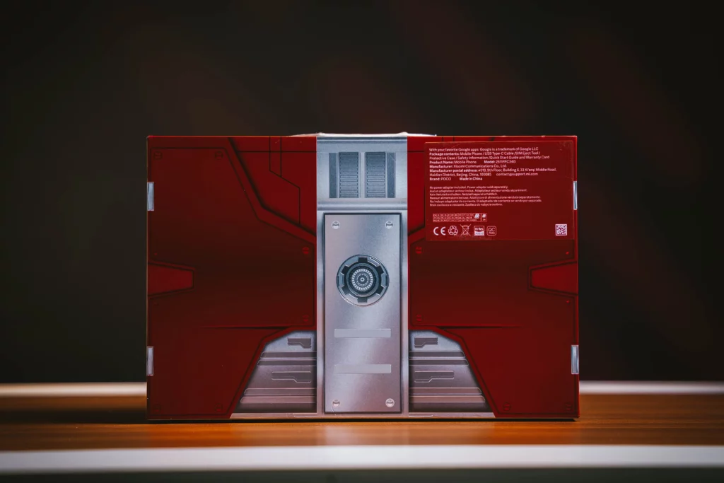 The POCO X8 Pro Iron Man Edition's box standing atop of a wooden table. The design resembling a suitcase.