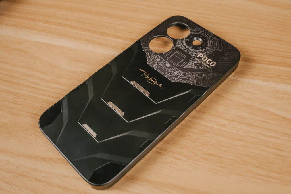 The POCO X8 Pro Iron Man Edition shown with its custom hard-shell case. The case is black with a textured, ridged bottom half and features "TONY STARK" written in gold script across the back.