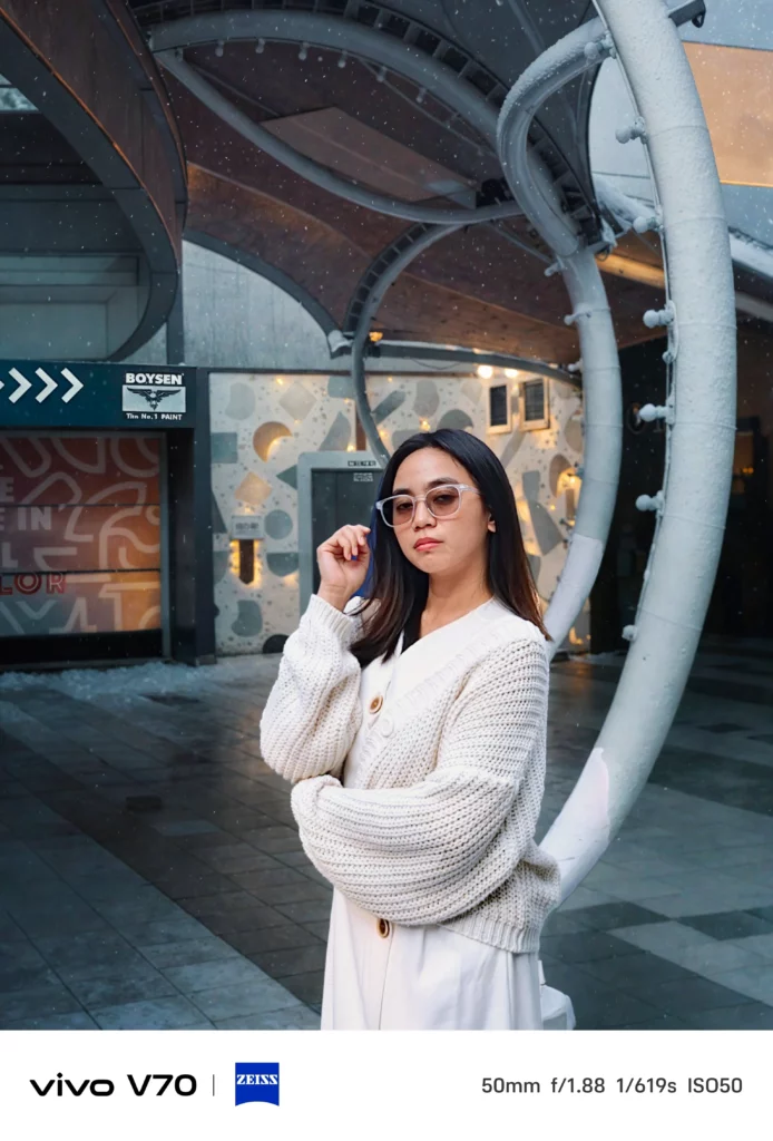 A portrait shot of the woman in a snowy or rain-flecked environment, demonstrating the camera's detail retention and color science in overcast conditions.