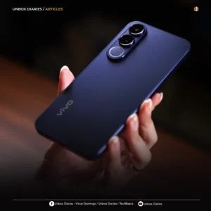 A person’s hand holding the vivo V70 FE at an angle, showcasing the smooth, matte purple finish and the prominent triple-camera module on the back. The lighting creates a soft gradient across the phone’s surface.