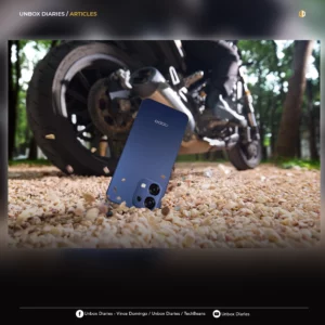 A promotional graphic for "Unbox Diaries" featuring the same action shot of the blue OPPO A6 Pro bouncing on gravel near a motorcycle. The image is framed with a dark gradient border and includes social media handles for Vince Domingo, Unbox Diaries, and TechBeans at the bottom.