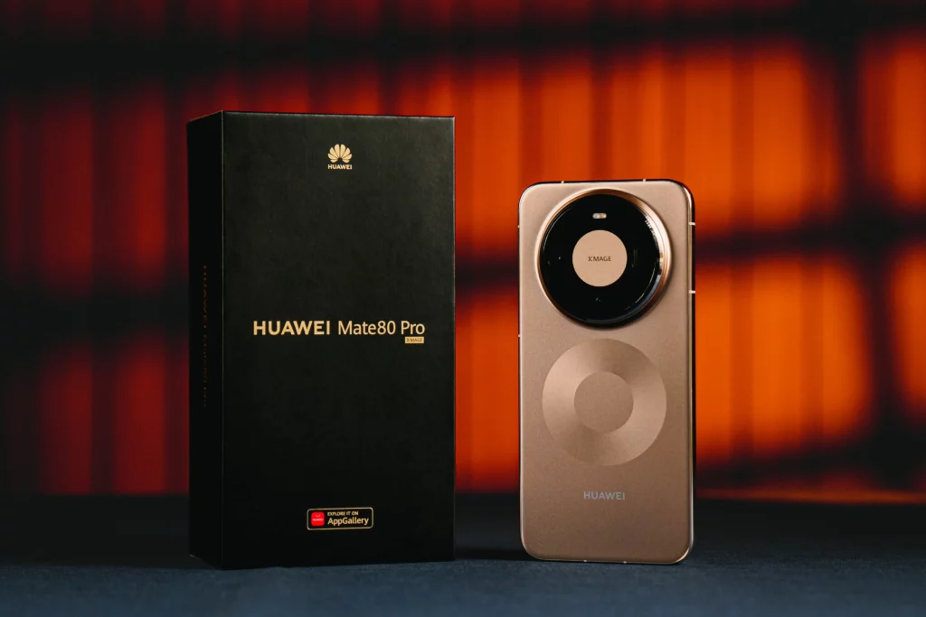 A premium matte black retail box for the HUAWEI Mate 80 Pro standing next to the device. The phone is shown from the back, featuring a metallic bronze finish and a prominent circular camera module.