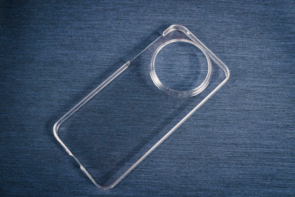 A top-down close-up of the included clear TPU protective case. The case features a large, precision-cut circular opening to accommodate the phone's signature camera array.