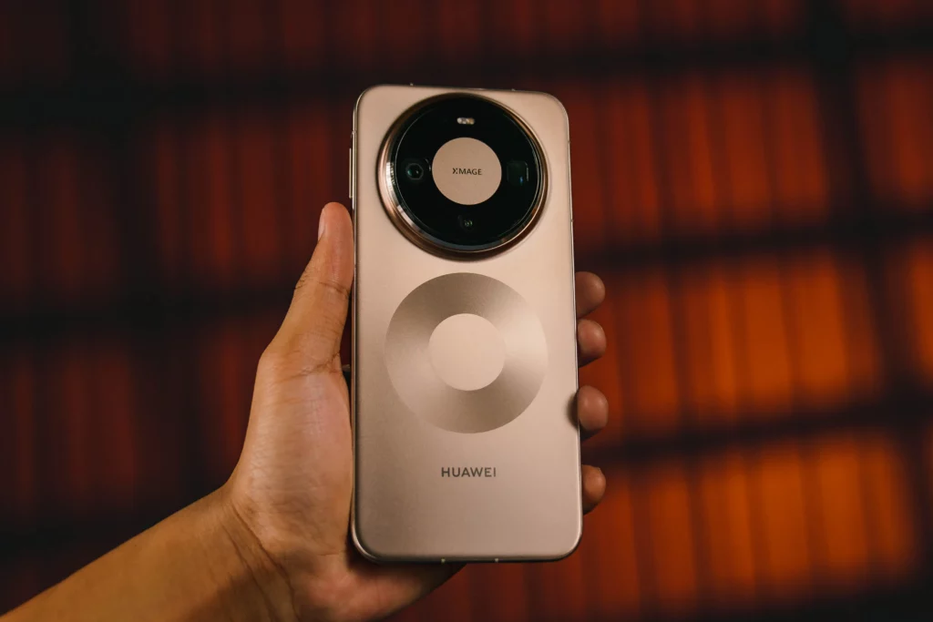 A hand holding the HUAWEI Mate 80 Pro, showcasing the ergonomic design and the large "XMAGE" branded circular camera island. The back panel has a unique concentric ring pattern etched into the bronze finish.
