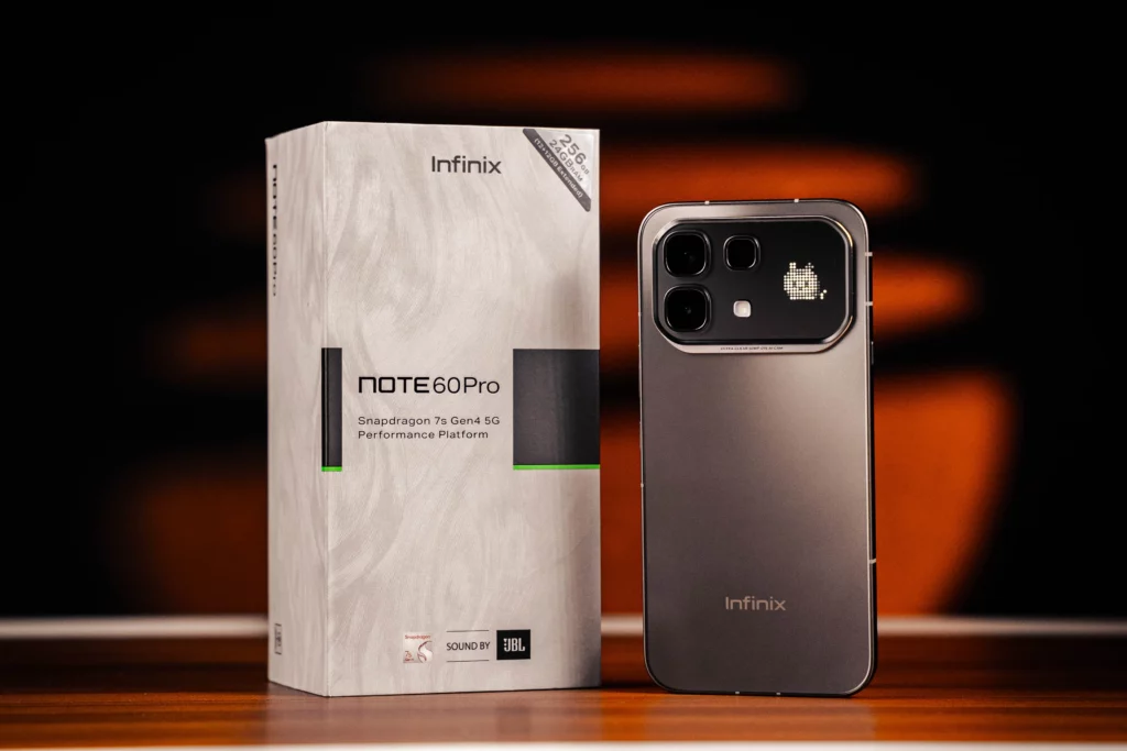 A sleek grey Infinix NOTE 60 Pro stands next to its white retail box. The phone's rear camera island features a unique "Active Matrix" dot-display showing a pixelated cat animation. The box highlights the "Snapdragon 7s Gen 4 5G" chipset and 256GB storage.