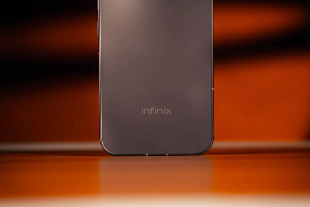A macro shot of the lower back of the Infinix NOTE 60 Pro, focusing on the clean, etched Infinix logo against the matte grey texture of the phone’s chassis.