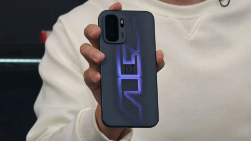 A person in a white sweatshirt holds a OnePlus Ace 6 Ultra smartphone vertically, showcasing its back design. The phone features a prominent rectangular camera module in the top left and a large, glowing purple graphic that resembles stylized geometric lines or letters stretching across the center. The lighting is soft, emphasizing the matte texture of the device.