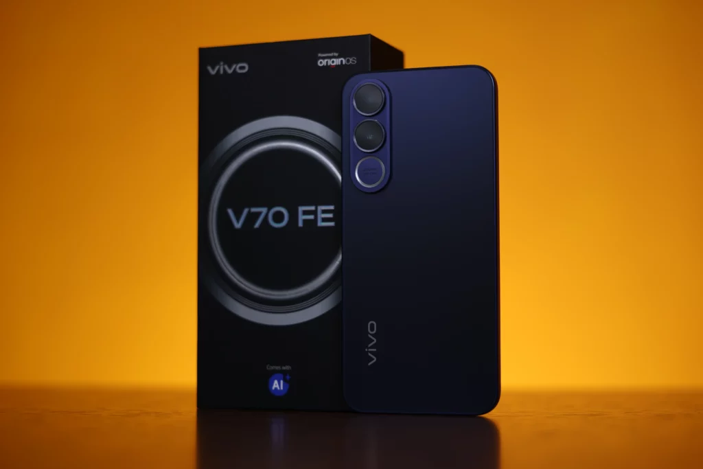 A back view of the vivo V70 FE in a deep matte purple, standing next to its black retail box. The phone features a vertical triple-camera setup with large circular lenses. The background is a solid, warm orange.