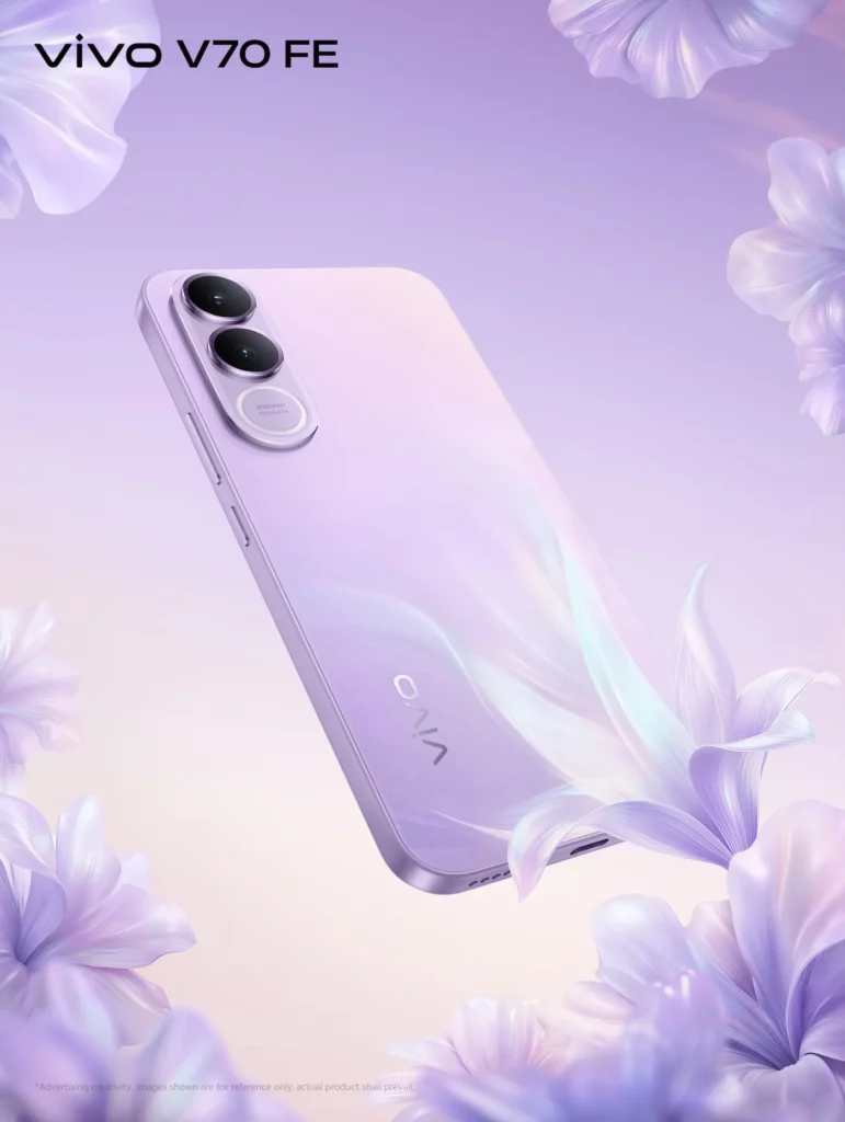 A close-up, angled view of the vivo V70 FE in Muse Purple. The back of the phone features a soft purple-to-pink gradient with a shimmering, silk-like texture. It is surrounded by floating, translucent purple flower petals that match the aesthetic of the device.