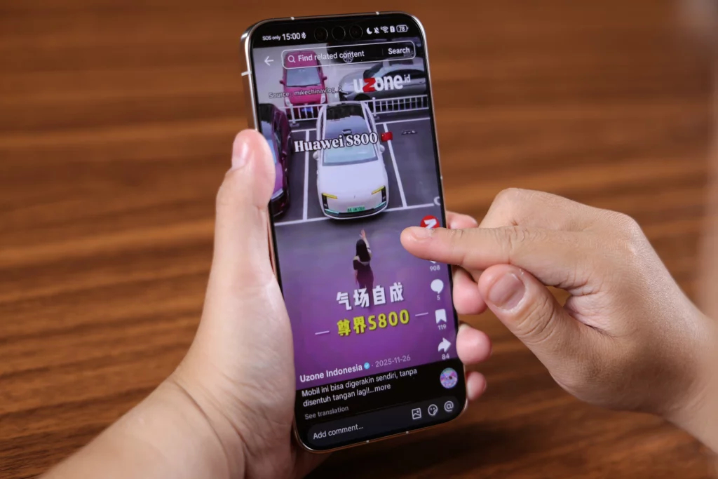 A person's hand holds a smartphone while an index finger interacts with the screen, which is playing a vertical video showing a "Huawei S800" autonomous luxury sedan parking itself. The video includes text overlays in Chinese and Indonesian text from an account named "Uzone Indonesia."