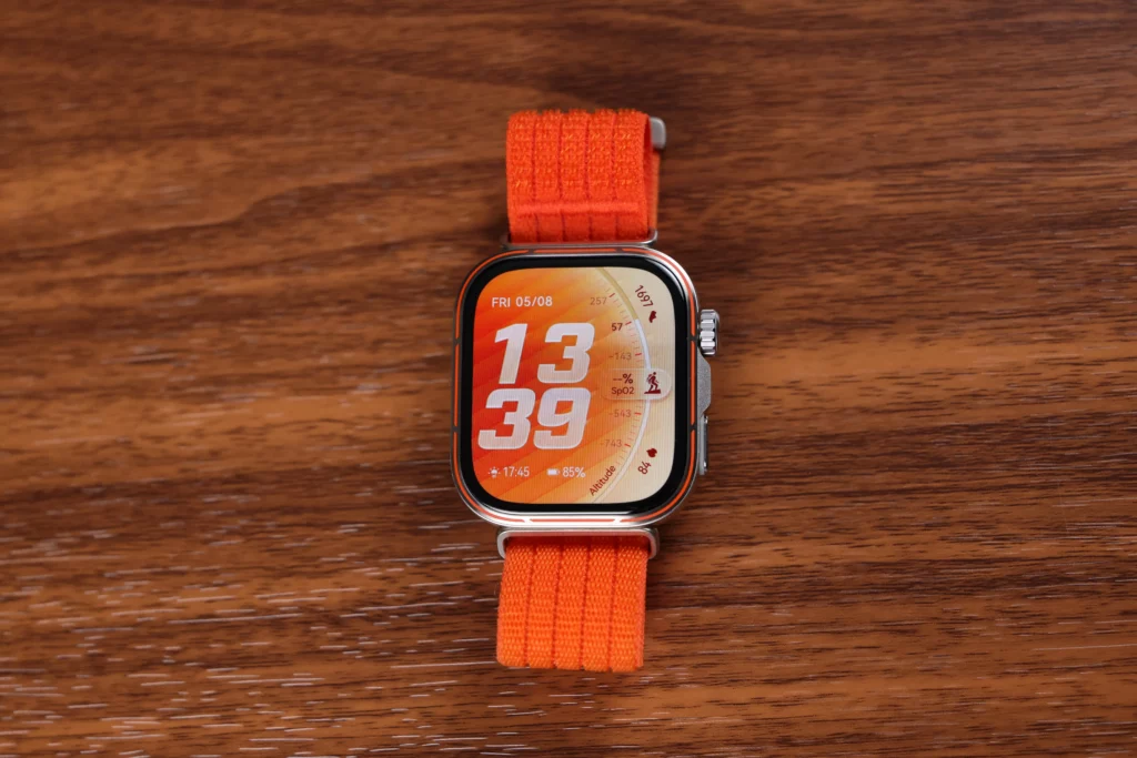A top-down view of the Huawei Watch Fit 5 Pro with its orange watch face and strap, displayed prominently against a wooden background.