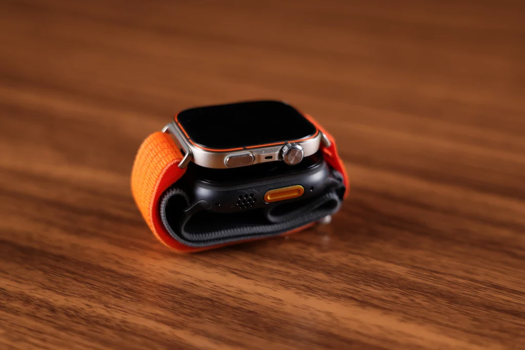 The Huawei Watch Fit 5 Pro (orange) stacked on top of the Apple Watch Ultra 3 (black) to show the difference in thickness and casing design.