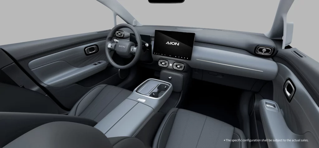 A high-angle view of the modern, tech-forward dashboard inside the GAC AION UT. The minimalist black and grey cockpit features a two-spoke steering wheel with the AION logo, an 8.88-inch digital instrument cluster, a large 14.6-inch central infotainment touchscreen displaying the AION logo, and a clean center console.