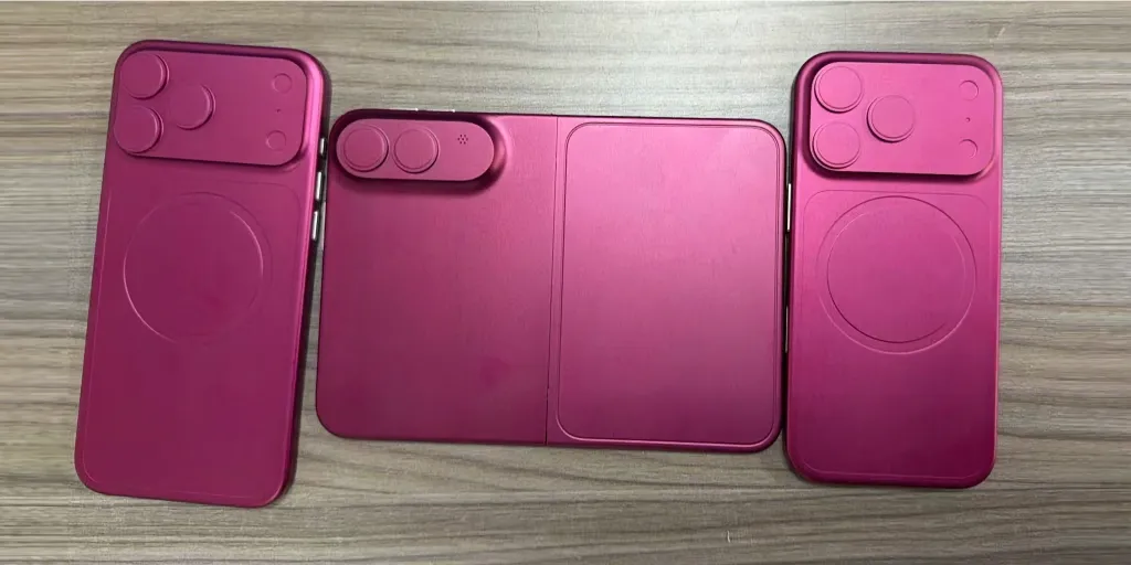 Three metallic, deep magenta or dark cherry prototype hardware molds laid out on a wooden surface. The left and right molds represent standard smartphone backs with triple-camera setups and circular MagSafe indicators. The center mold shows a book-style folding smartphone design in its unfolded state, featuring a dual-camera module on its left pane.