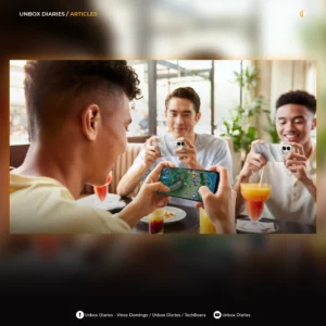 A digital article graphic featuring a framed lifestyle image of three young men at a restaurant table using smartphones—one playing a mobile game in the foreground and two holding textured silver devices in the background. The graphic includes a dark blurred border, the text "UNBOX DIARIES / ARTICLES" in the top-left corner, a gold logo in the top-right corner, and social media handles for Facebook and YouTube at the bottom.