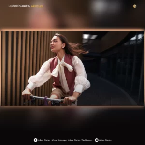 A graphic header for Unbox Diaries featuring a woman with flowing hair riding a bicycle while wearing an earbud in an urban setting.