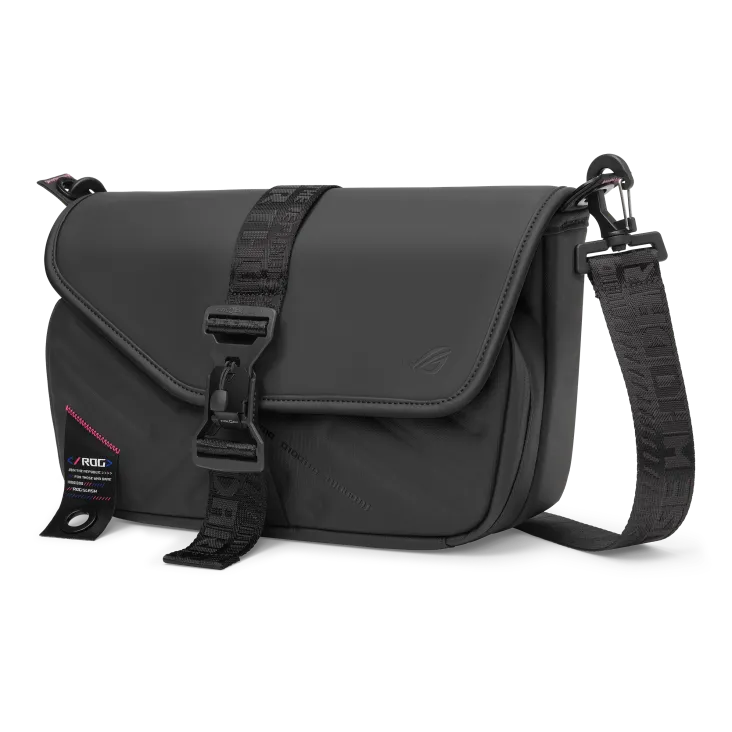 A close-up studio shot of a black ROG Slash Sling Bag 4.0 against a white background, featuring a heavy-duty buckle, patterned utility straps, and a small hanging brand tag with pink and blue accents.