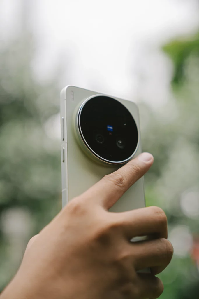Close-up shot focusing on the rear design of the light green vivo X300 Ultra held up in a hand. The design emphasizes the massive, elevated circular camera housing with multiple lenses and a distinct blue ZEISS brand badge against a soft-focus green background.
