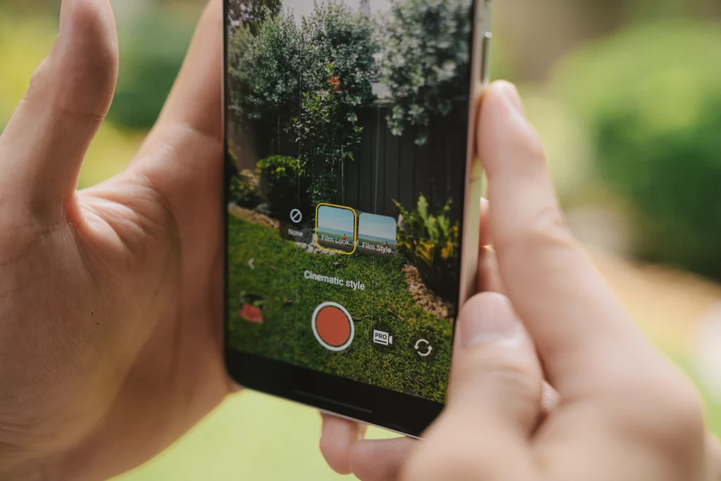Close-up profile view of hands holding the vivo X300 Ultra while using the video camera app. The interface displays "Cinematic style" options with "Film Look" selected next to a large red record button, framing an outdoor garden scene.