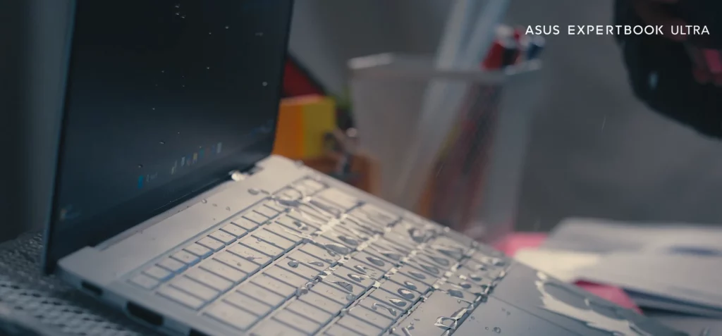 Close-up side view of a silver ASUS ExpertBook Ultra keyboard with water droplets splashed across the keys, demonstrating its splash-resistant feature.