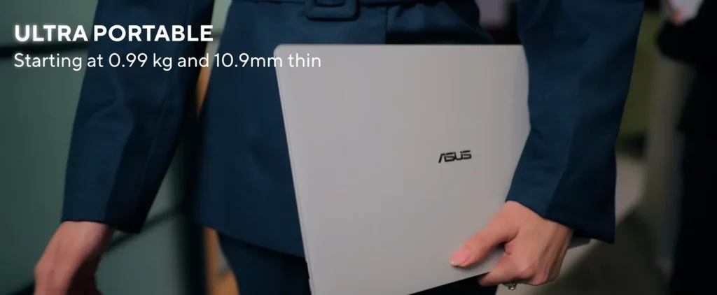 Close-up of a person in a professional navy blue suit carrying a slim gray ASUS ExpertBook Ultra laptop under their arm, with text reading "ULTRA PORTABLE - Starting at 0.99 kg and 10.9mm thin".