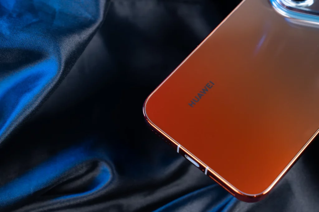 Close-up of a smartphone's glossy metallic bronze back panel featuring the Huawei logo, resting on dark blue draped fabric.