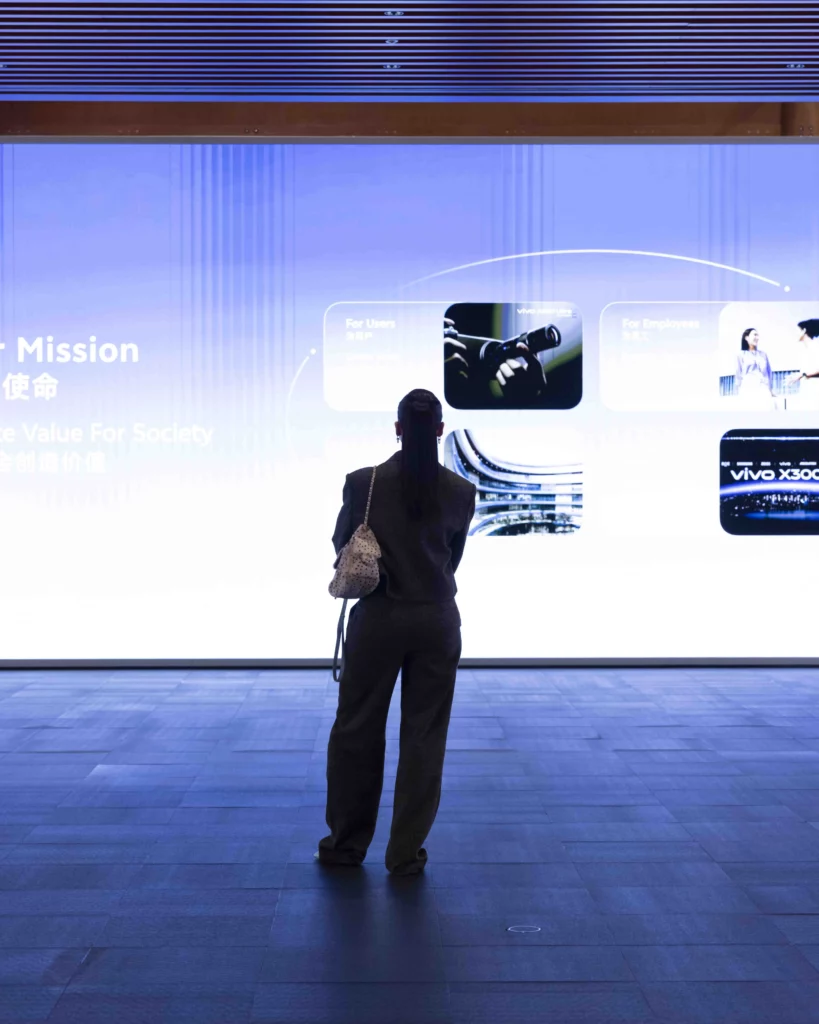 Full-length view from behind of Anne Curtis standing in front of a massive glowing digital screen displaying vivo's mission statement and photos of the X300 series products.